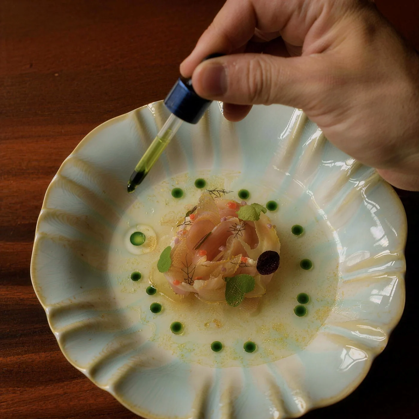 A chef adds drops of oil with a pipette to a rose of sliced fish