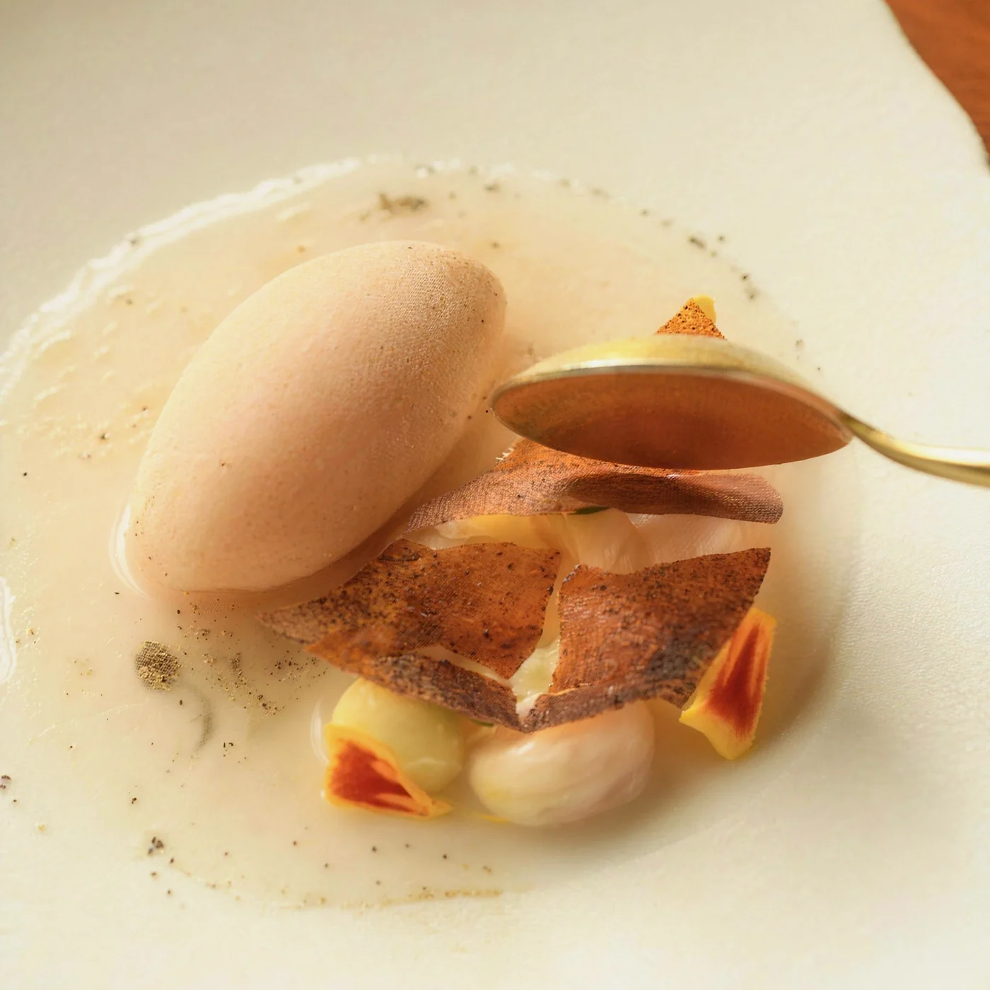 Quenelle of ice cream beside a crisp tuile, with sauce spooned over at the pass
