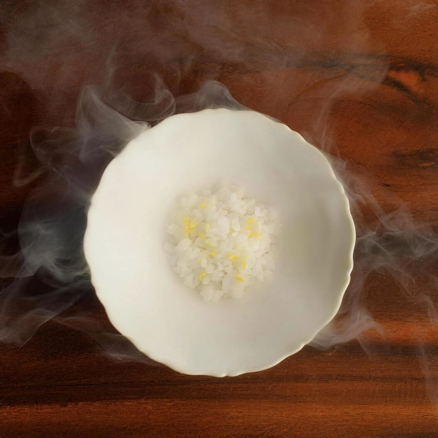 White granita with citrus zest in a fluted bowl, wrapped in cold vapour on a dark wood counter