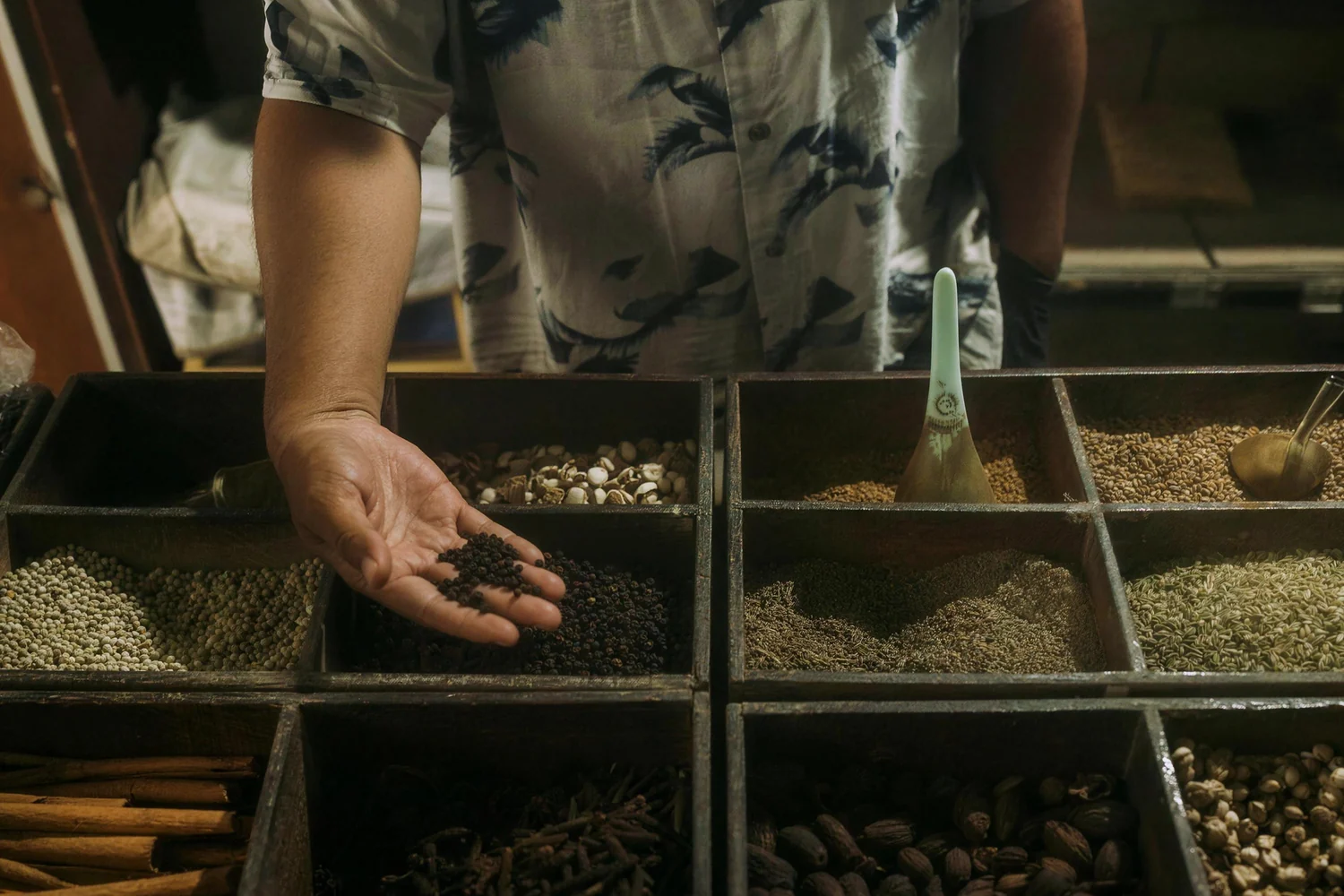 A hand holding dried spices over a market stall of spice trays