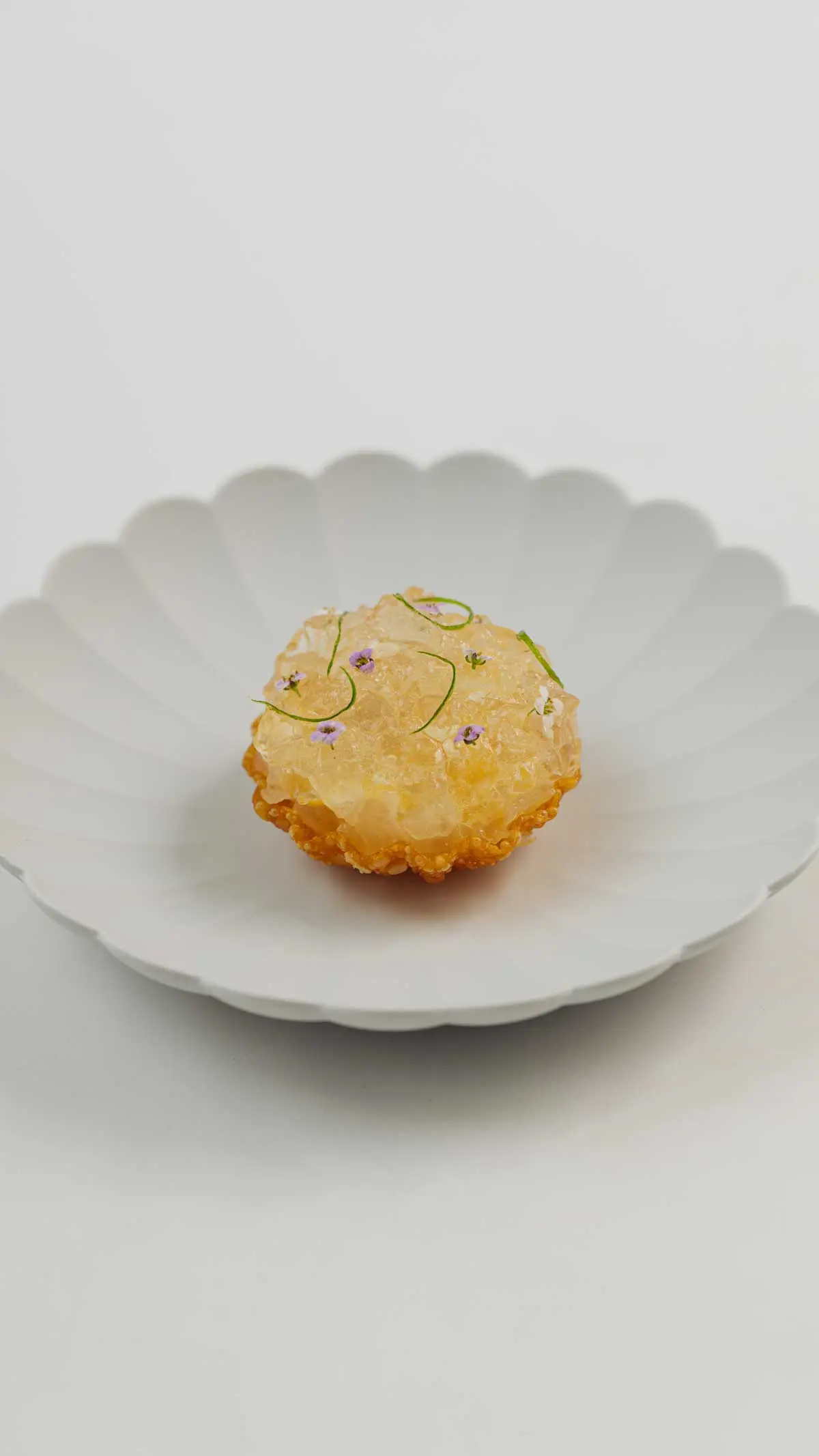 Golden fritter glazed and dressed with purple edible flowers and chive curls, on fluted white china