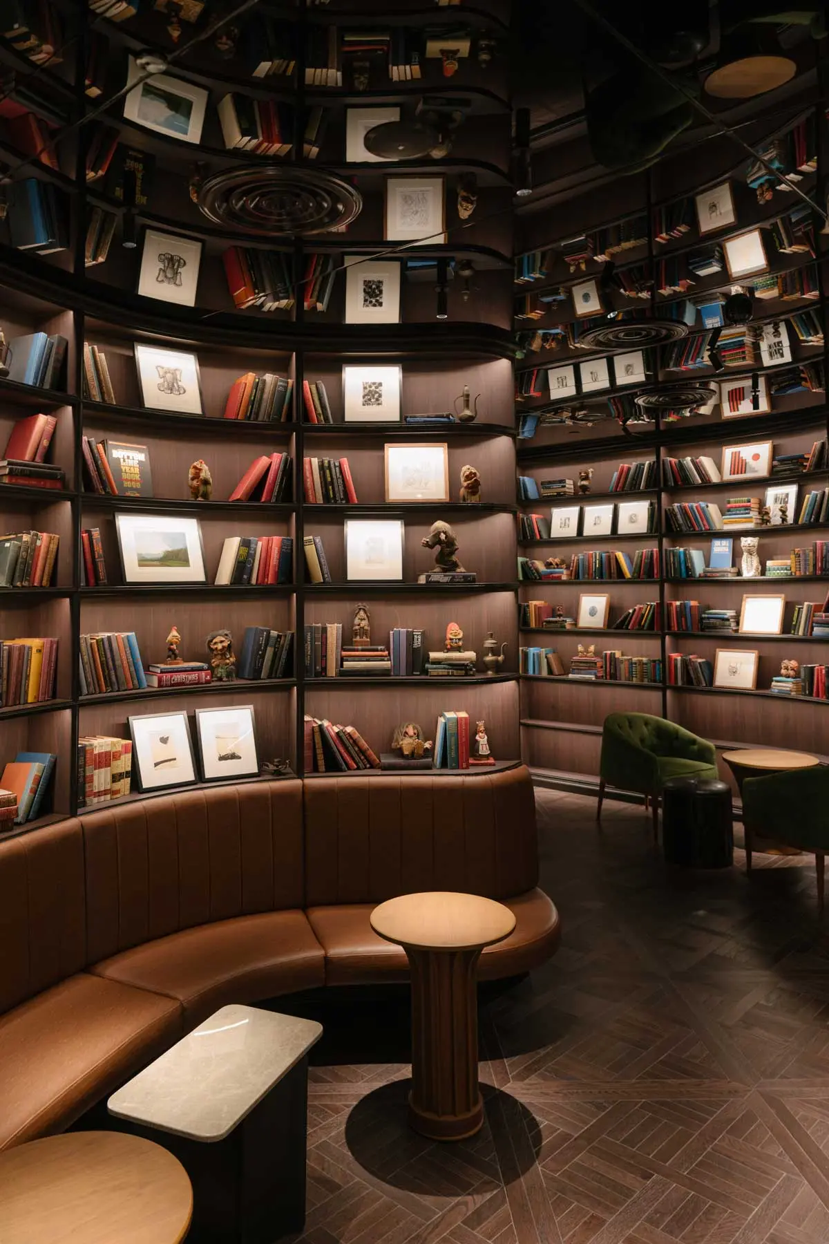 Circular library lounge lined with books and framed art, curved leather banquette and herringbone floor
