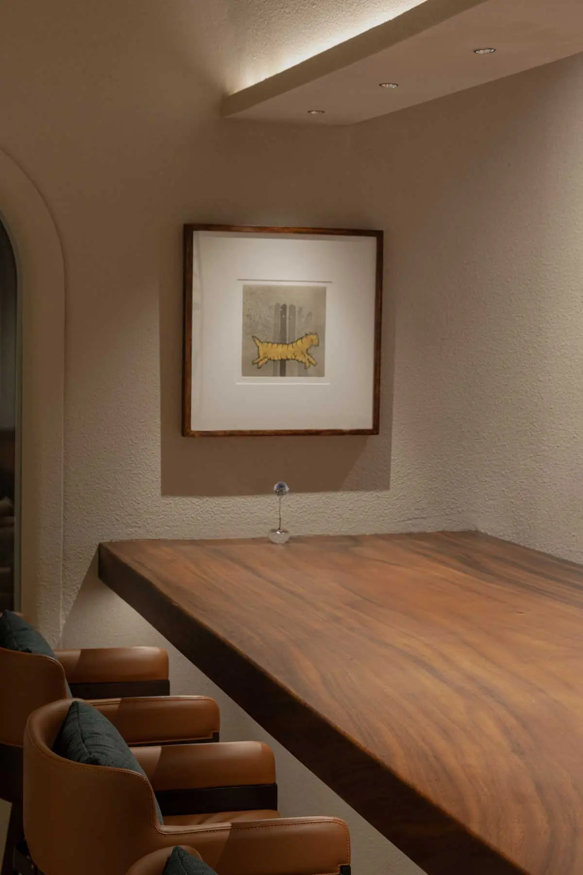 Live-edge wooden counter beneath a framed yellow tiger drawing, tan leather armchairs alongside